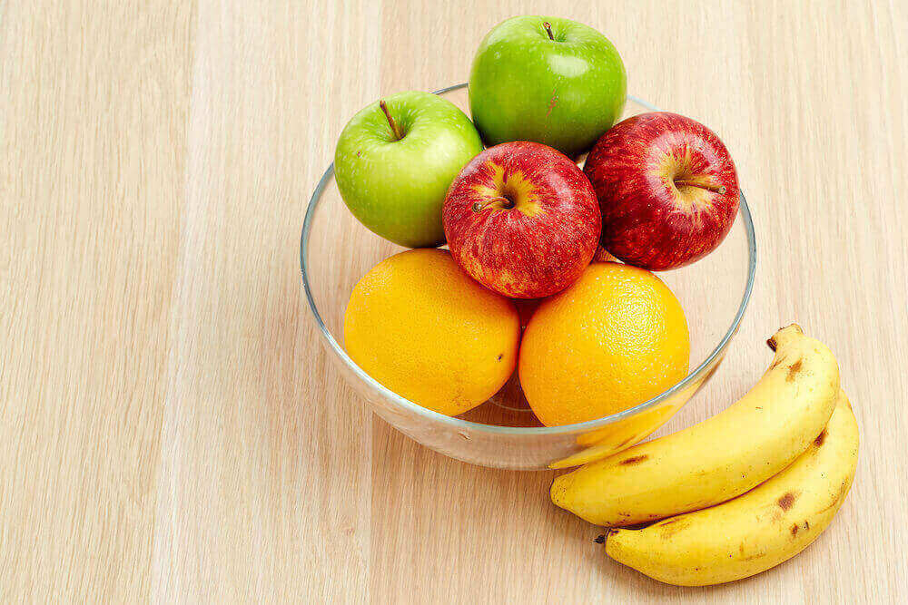 clear glass bowl of oranges and apples next to bananas on a wooden table